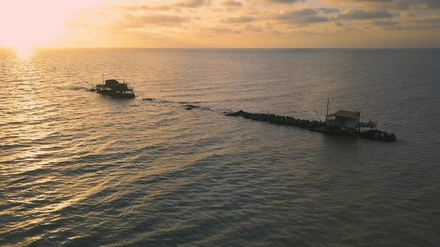 Vista aerea di sagome dei trabucchi sul mare per la pesca del pesce con pescatori alle ultime luci del tramonto.