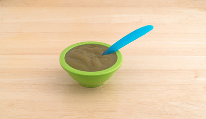 Bowl of organic spinach baby food with a spoon in the food on a wood table.