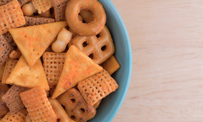 Top close view of snack crackers and pretzels in a green bowl atop a wood table.