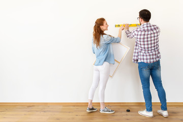 Couple in empty apartment measuring walls. Activities after relocation and renovation.