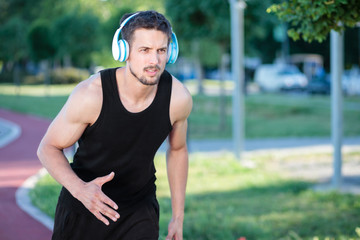 Fototapeta premium Determined young man running in a park, wearing wireless headphones. Exercising in urban environment.