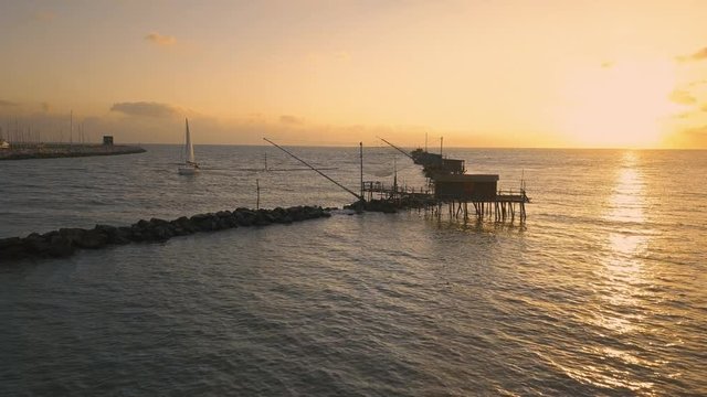 Vista aerea di sagome dei trabucchi sul mare per la pesca del pesce con pescatori alle ultime luci del tramonto.
