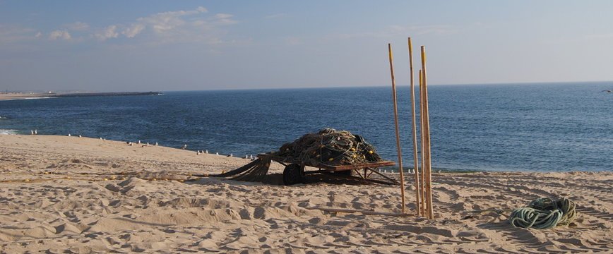 Redes de pesca recolhidas e colocadas em cima de um reboque para transporte, paus de apanhar as rede ao alto espetados na areia da praia