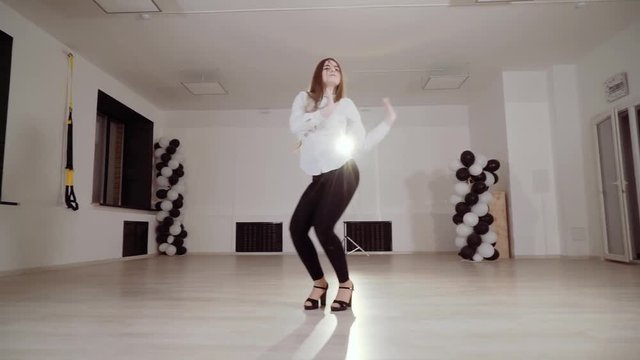 A girl in a white blouse rehearsing a dance in the studio.
