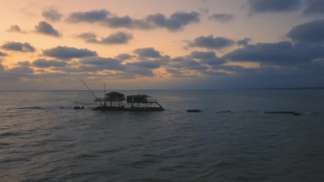 Vista aerea di sagome dei trabucchi sul mare per la pesca del pesce con pescatori alle ultime luci del tramonto.