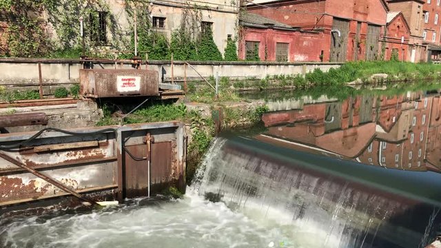 Close up of a cascade in a mirrored canal with a lock near an old factory in a sunny day in Certosa di Pavia, Italy.