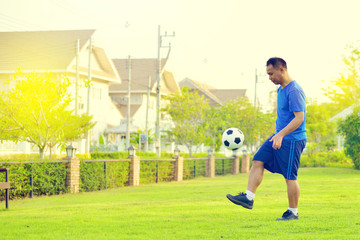 Asian fat man playing football alone in garden
