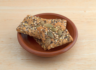 Whole wheat seeded crackers in a small bowl on a wood table.