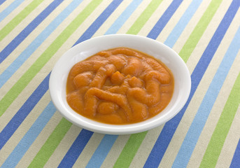 Bowl of organic pumpkin and carrot baby food on a striped tablecloth.