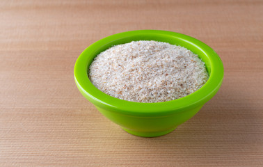 A small green bowl filled with psyllium husks on a wood table.