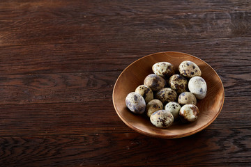 Fototapeta na wymiar Fresh quail eggs in a wooden plate on a dark wooden background, top view, close-up