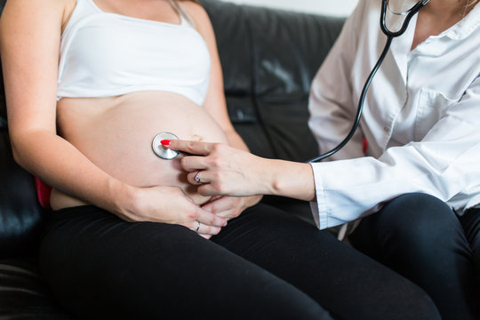 Doctor checking pregnant woman with stethoscope.