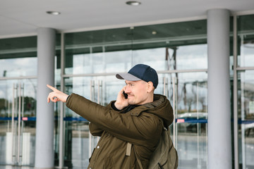 A young male tourist at the airport or near a shopping center or station calls a taxi or talks on a cell phone or communicates with friends using a mobile phone