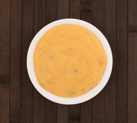 Top view of melted dipping cheese in a small white bowl atop a brown wood place mat.