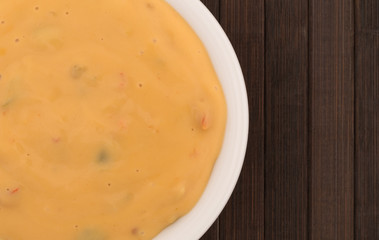 Top close view of melted dipping cheese in a small white bowl atop a brown wood place mat.