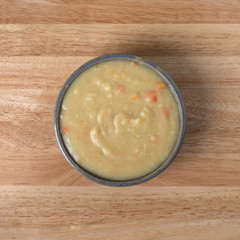 Home style potato soup in a stoneware bowl atop a wood table illuminated with window light.