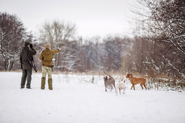 two hunters with rifles in a snowy winter forest.