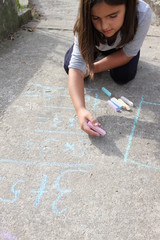 Girl kid thinking, writing and counting on mathematical equations with colored chalks on a pavement. School and vacation concept. Education concept. School and fun time.