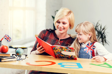Female blonde english teacher reading book with smart kid girl, language child studying process in...