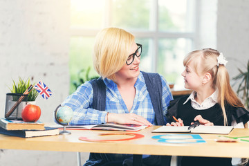 English language female teacher studying with smart kid girl in light white classroom, children learning concept