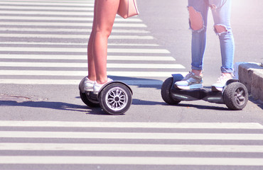 Two girls on gyro boards stops on a pedestrian crosswalk