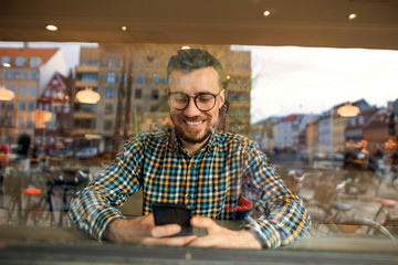 Obraz premium fashion guy with glasses and checkered shirt sitting in a cafe working in the phone