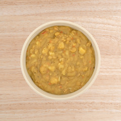 Top view of yellow split pea and vegetable soup in a bowl on a wood table.