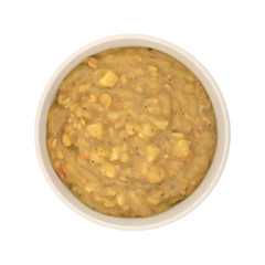 Top view of a bowl of yellow split pea and vegetable soup on a white background.