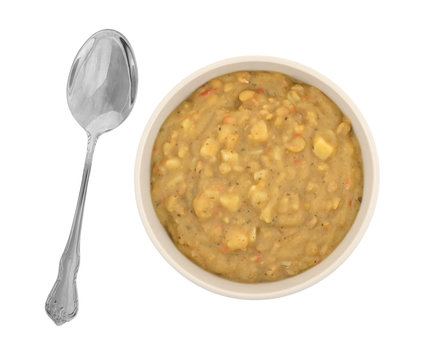 Top View Of Yellow Split Pea And Vegetable Soup In A Bowl With A Spoon To The Side Isolated On A White Background.