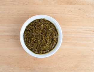Top view of a bowl of chopped parsley in canola oil on a wood table.