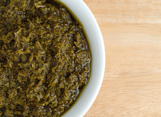 Top close view of a bowl of chopped parsley in canola oil on a wood table.
