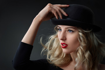 Low key portrait of glamour blond woman, wearing a hat, studio shot, blurred background, day light