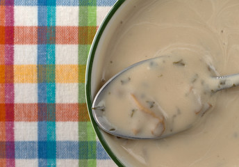 Top close view of creamy mushroom soup in a bowl with a spoon atop a colorful place mat illuminated with natural light.