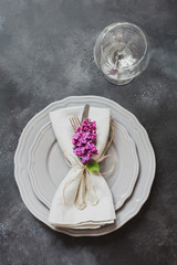 Table place setting with pink lilac flowers, silverware on vintage background. View from above. Copy space.