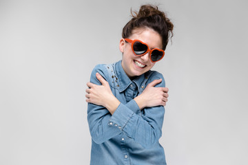 Young brunette girl with glasses in the form of a heart. The hairs are gathered in a bun. The girl is hugging herself with her hands.