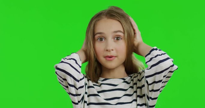 Close up of the cute teen girl with long hair in the striped blouse holding her head with hands and doing surprised or scarry face. Green screen. Chroma key