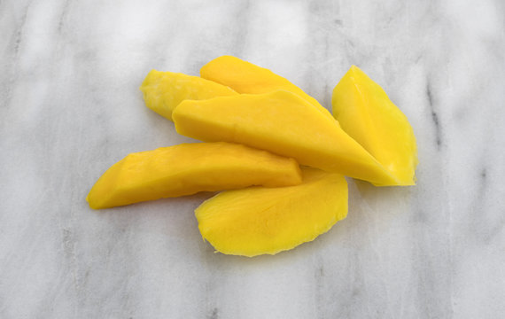 Slices of fresh mango on a marble cutting board.