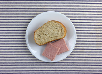 Top view of a pressed pork canned meat sandwich on wheat bread on a white plate atop a blue striped tablecloth.