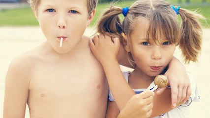 Cute little Latin girl and Caucasian boy necking with a colorful candies in mouths on tropical beach vacation