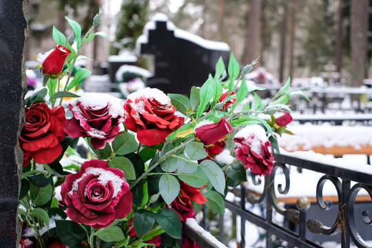 Artificial flowers bouquet of roses on the grave in the winter. Cemetery decorations. Selective focus.