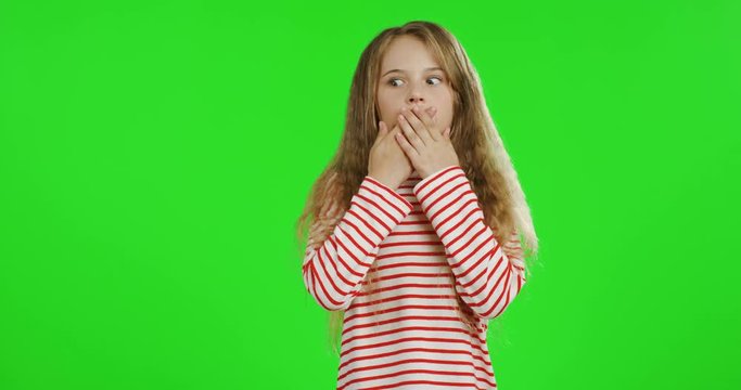 Portrait of the blonde teenager girl with long hair in the striped blouse closing her mouth with hands and doing oops grimacing or very surprised face. Green screen. Chroma key