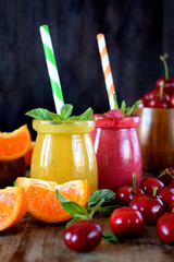 Yellow and red smoothies in glass jars surrounded by mandarins and cherries