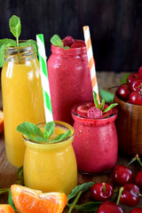 Yellow and red smoothies in glass jars surrounded by mandarins and cherries