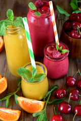 Yellow and red smoothies in glass jars surrounded by mandarins and cherries