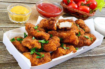 Chicken nuggets. Pieces of deep-fried crispy meat,  with different sauces on a wooden table. Traditional snack.