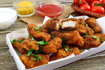 Chicken nuggets. Pieces of deep-fried crispy meat,  with different sauces on a wooden table. Traditional snack.