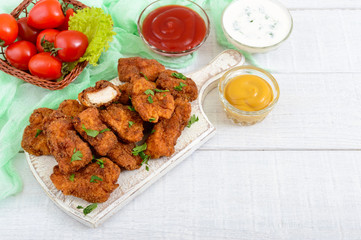 Chicken nuggets. Pieces of deep-fried crispy meat, on paper with different sauces on a white wooden table. Traditional snack.