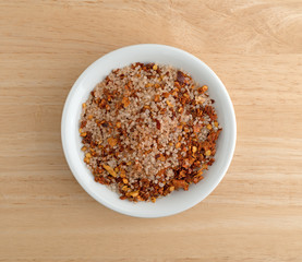 Top view of Greek spice rub in a white bowl atop a wood table.