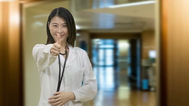 Asian female doctor showing thums up in hospital hallway wards