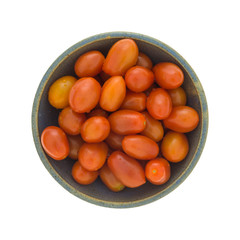 Top view of an old stoneware bowl filled with grape tomatoes on a white background.